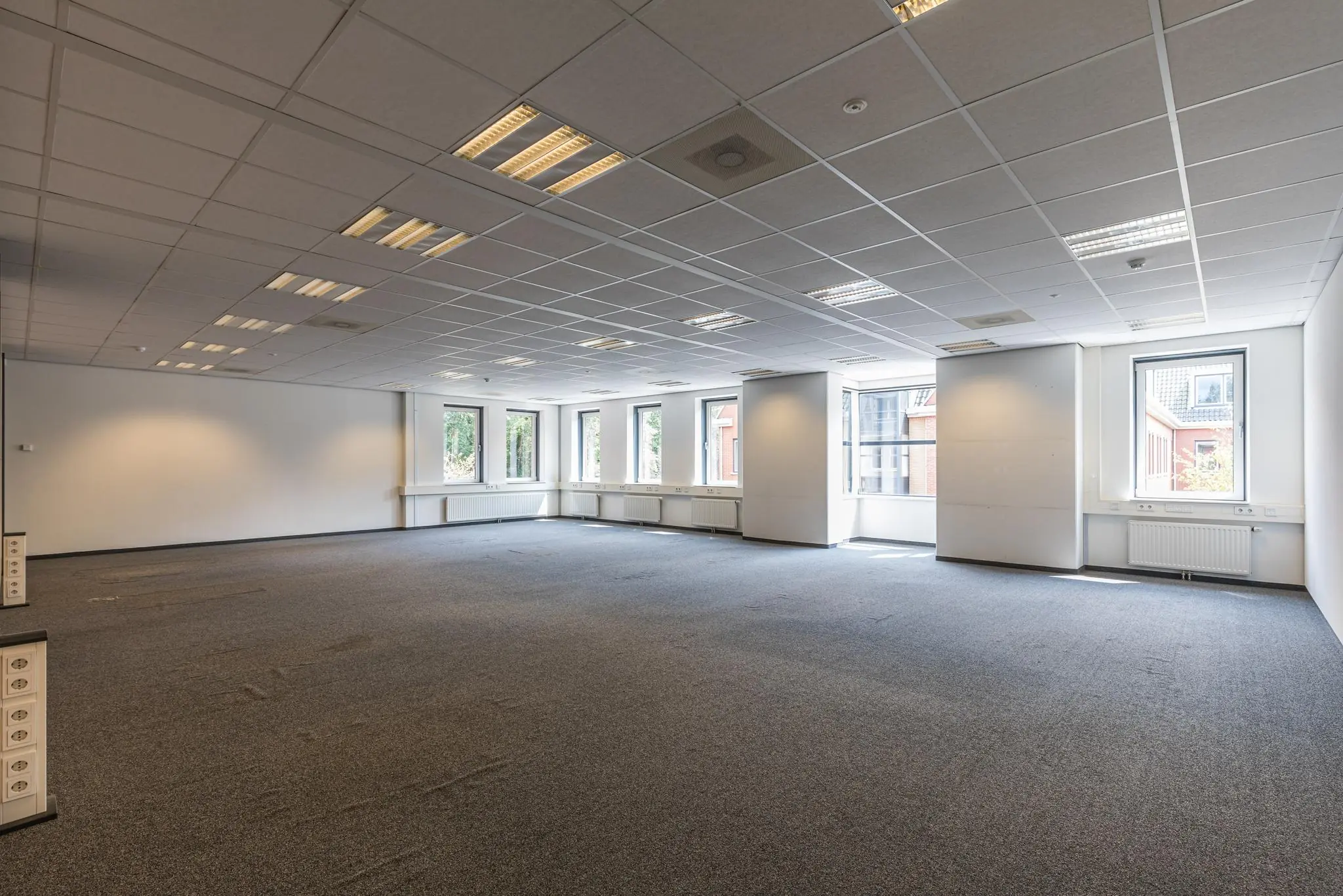 Leeg kantoorpand aan de Laan Blussé van Oud-Alblas met tapijtvloer, systeemplafond en meerdere ramen voor natuurlijk licht.